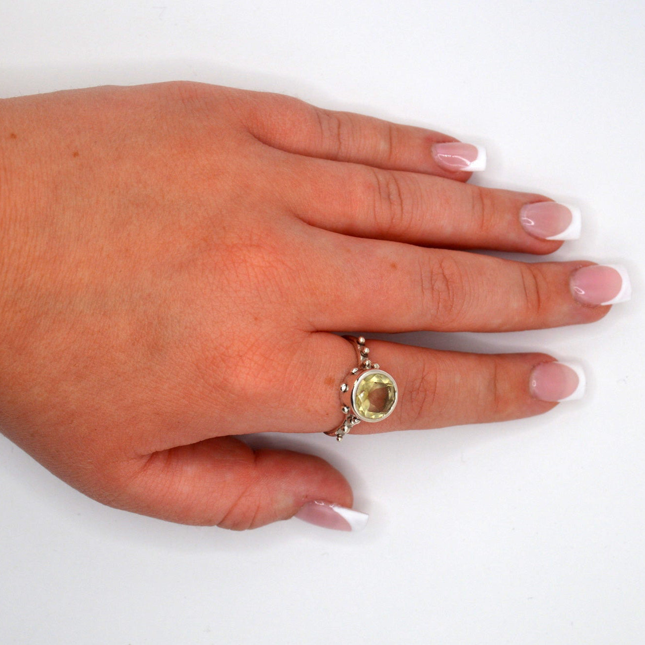 Hand wearing a ring with a yellow gemstone on a white background