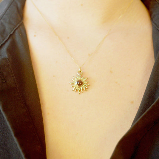 Close-up of a necklace with a sun design on a person wearing a black jacket.