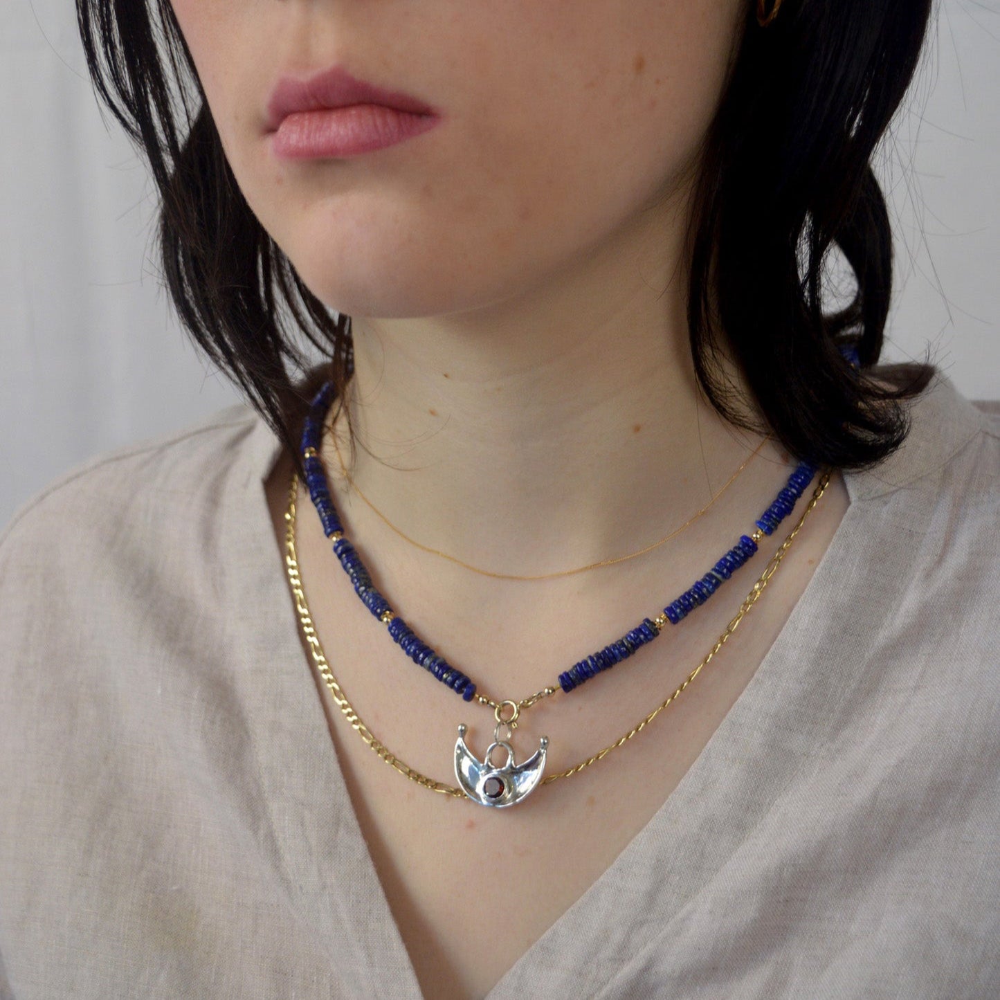 Close-up of a person wearing two necklaces with a plain background