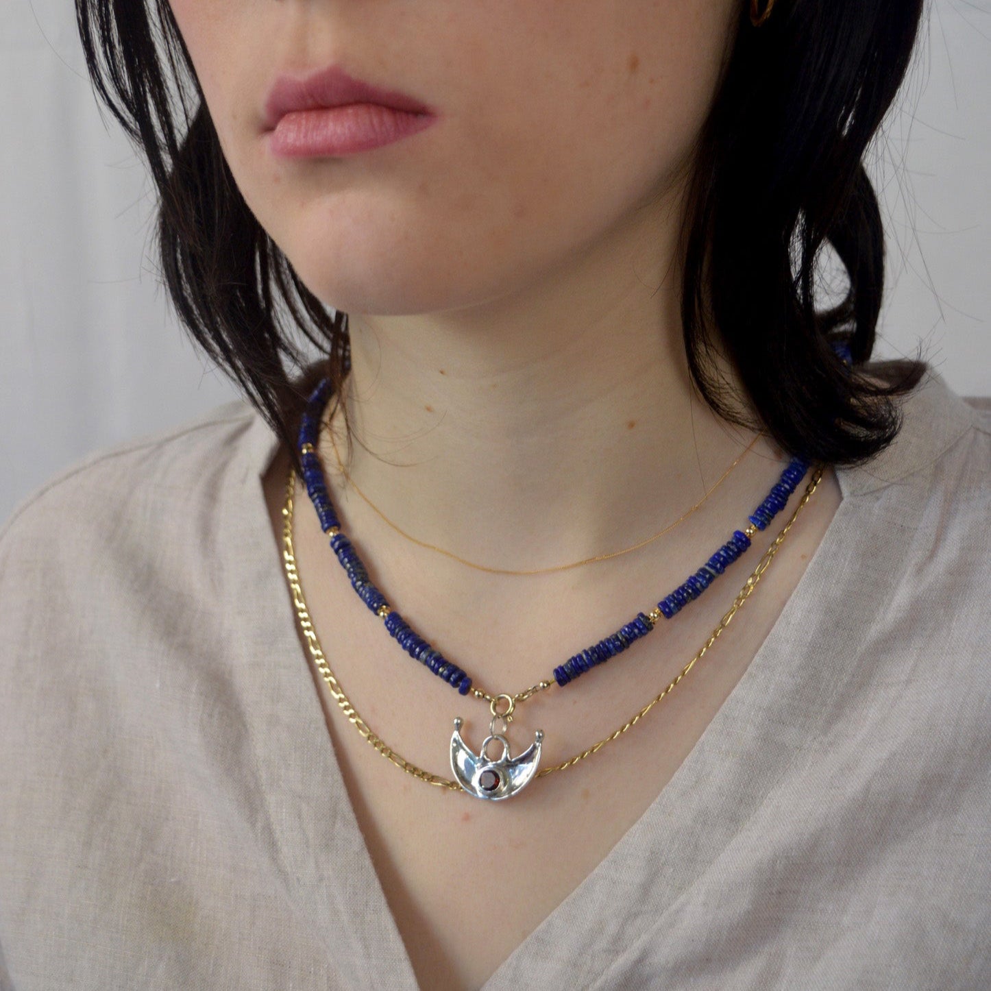 Close-up of a person wearing two necklaces with a plain background