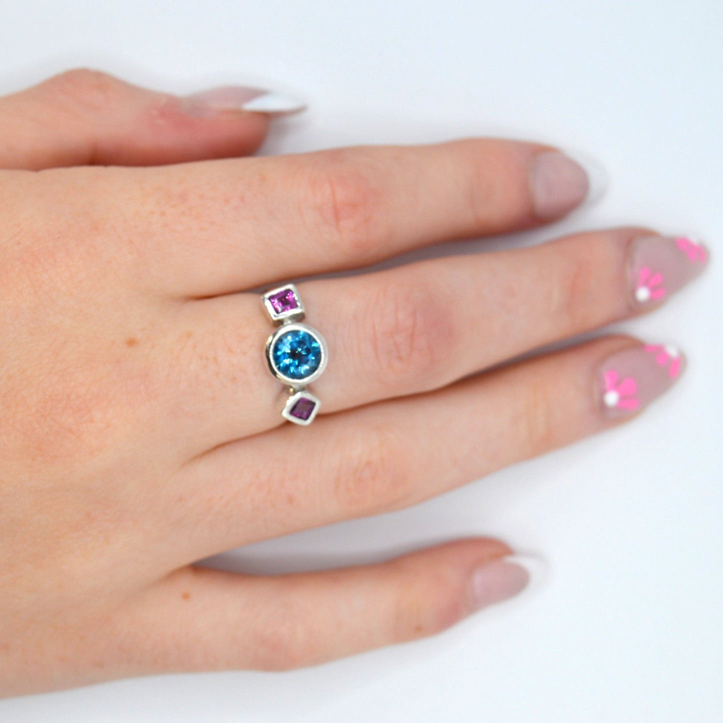 Hand wearing a ring with a blue gemstone on a white background