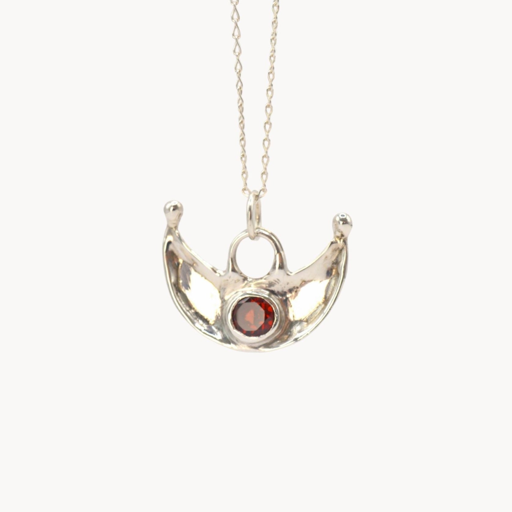 Silver necklace with a pendant featuring a red gemstone on a white background