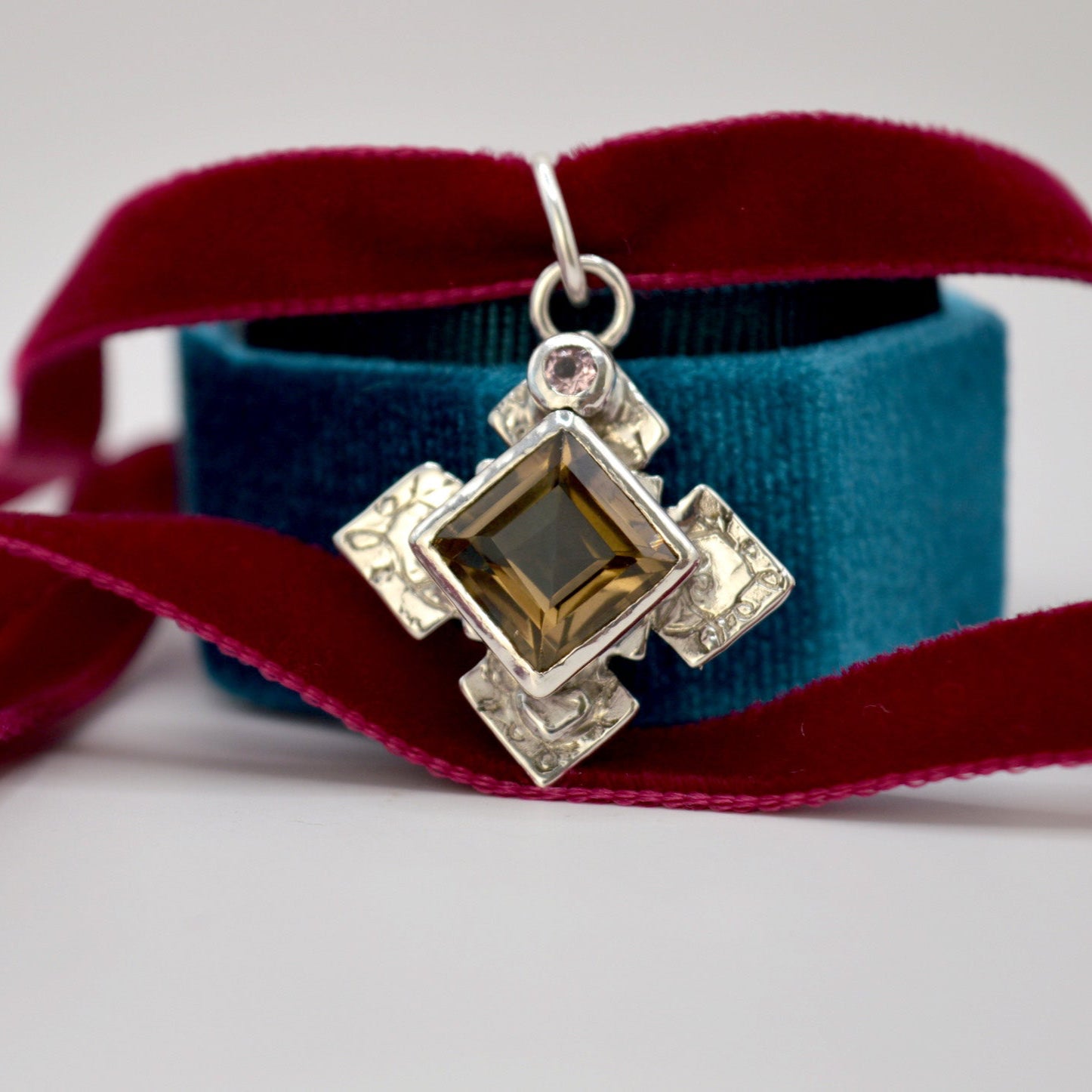 Silver pendant with a brown gemstone on a red ribbon against a blue box background