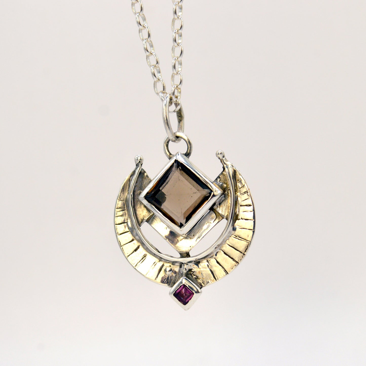 Necklace with a pendant featuring a square gemstone and a circular design on a white background