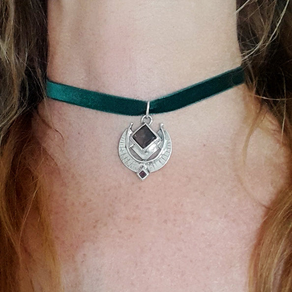 Person wearing a green velvet choker with a silver pendant featuring a brown stone.