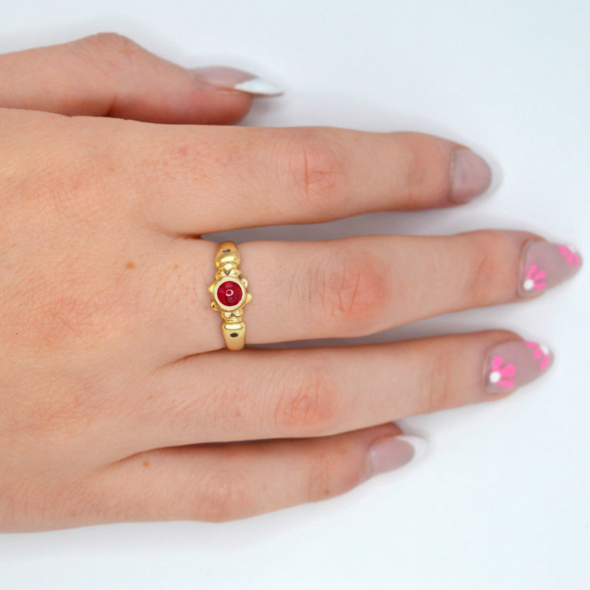 Gold ring with a red gemstone on a hand against a white background