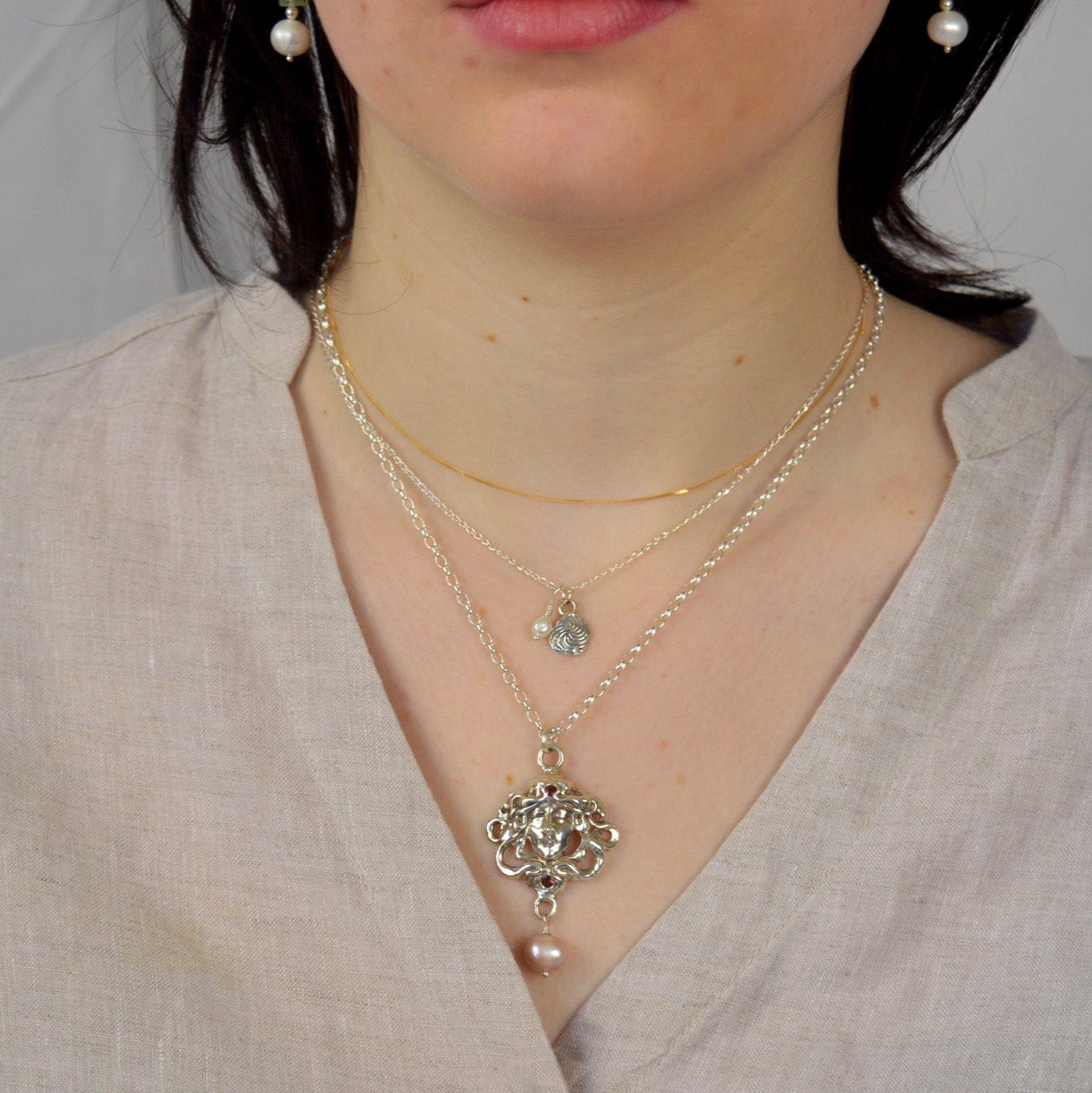 Person wearing a light-colored shirt with a necklace and earrings against a plain background