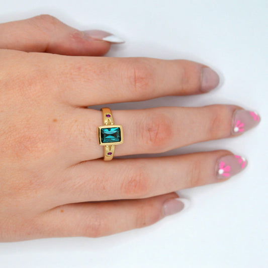 Hand wearing a gold ring with a green gemstone on a white background