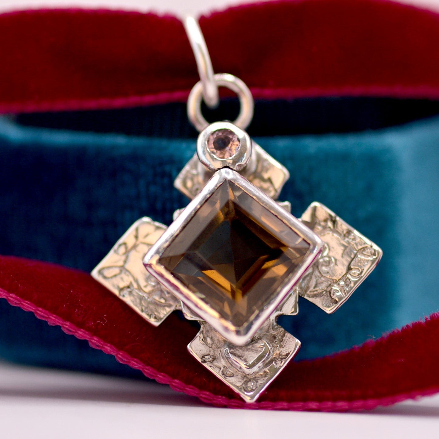 Silver pendant with a large brown gemstone on a red and blue fabric background