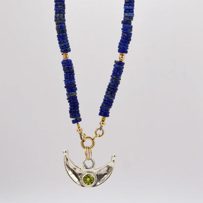 Necklace with blue beads and a silver crescent moon pendant on a white background