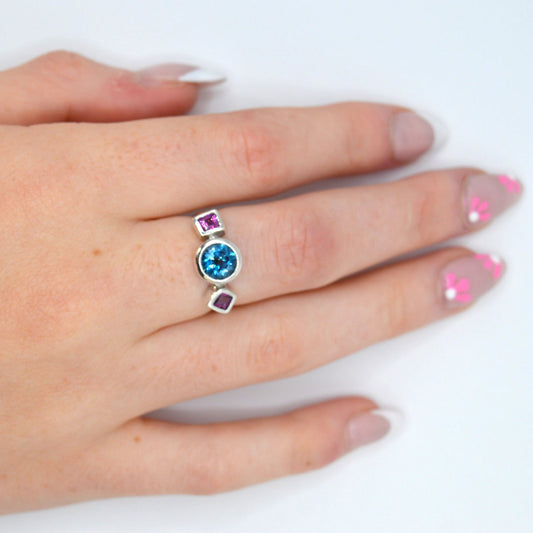 Hand wearing a ring with a blue gemstone on a white background