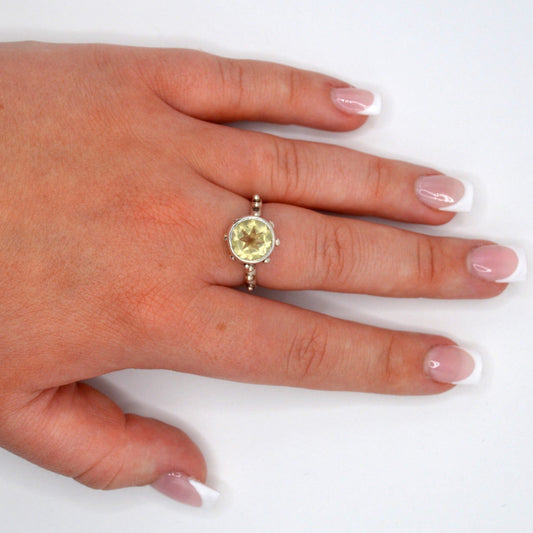 Hand wearing a ring with a yellow gemstone on a white background
