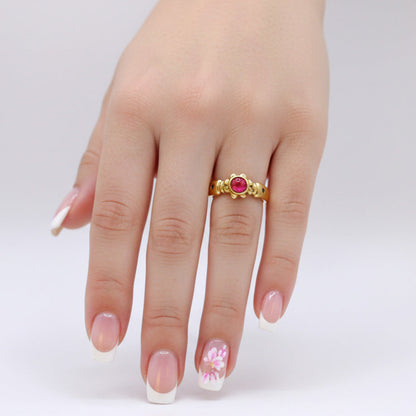 Gold ring with a red gemstone on a hand against a white background