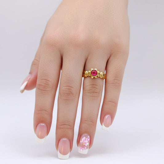 Gold ring with a red gemstone on a hand against a white background